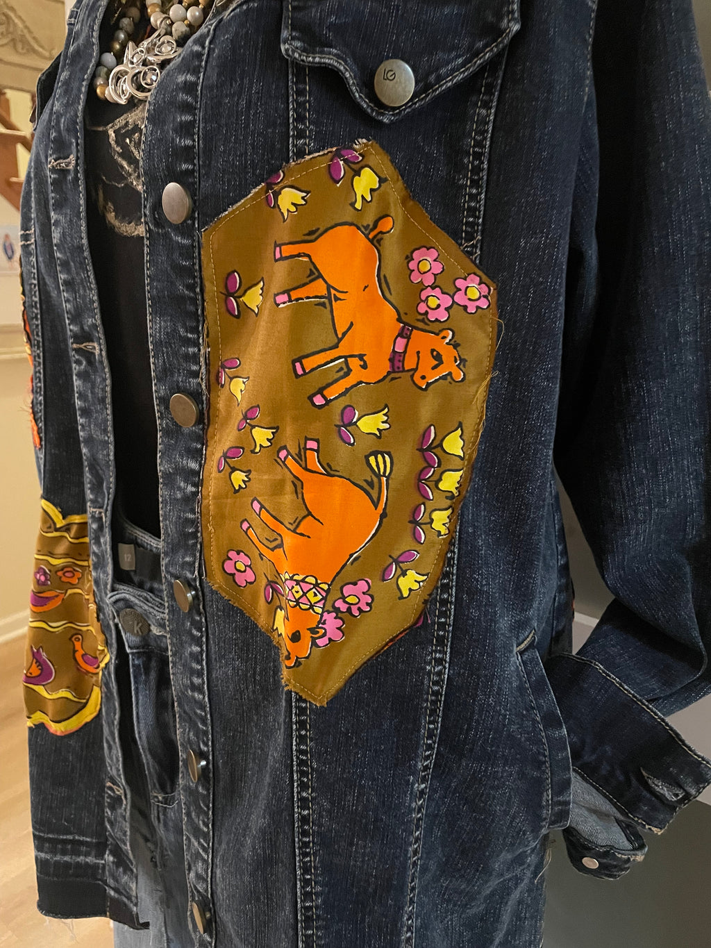 Denim jacket with a decorative patch featuring orange cows and flowers.